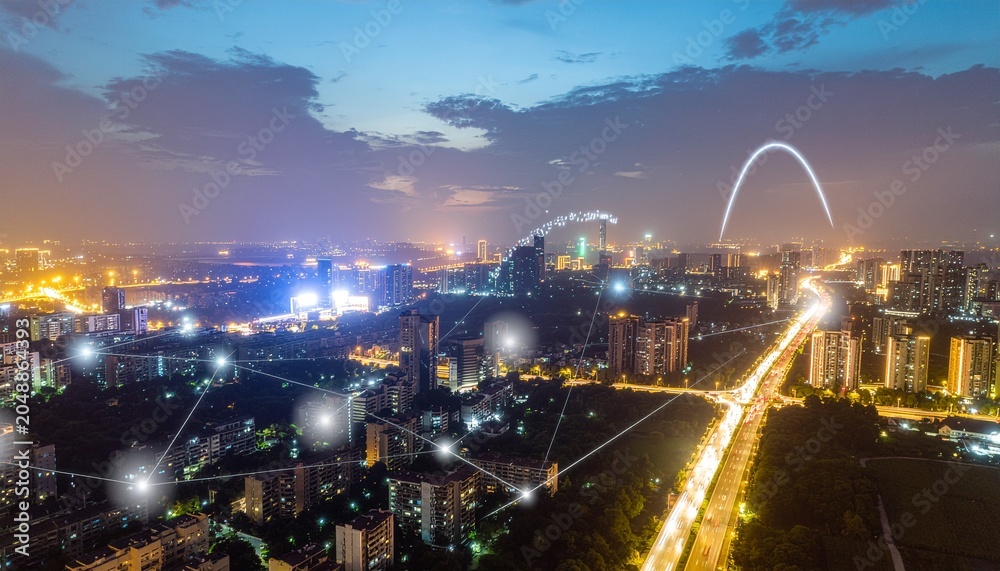 Obraz premium Aerial night view of a city skyline with glowing network nodes and light trails on the highway