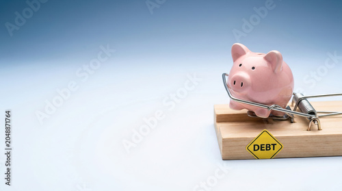 Pink piggy bank caught in mousetrap labeled debt symbolizes life cycle of financial investing and cost of falling into debt traps that hinder economic growth and savings