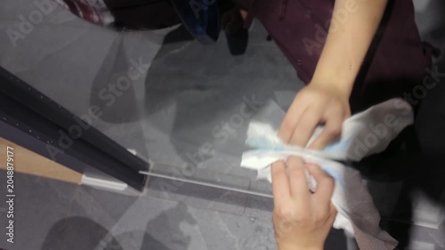 A teenage girl sprays cleaner and wipes a mirrored wardrobe door with a paper towel during household chores in a home hallway.