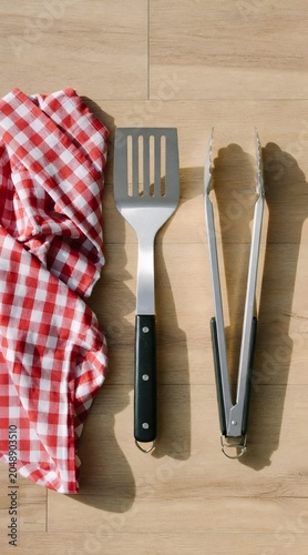 BBQ spatula and tongs with red checkered napkin on a wooden table