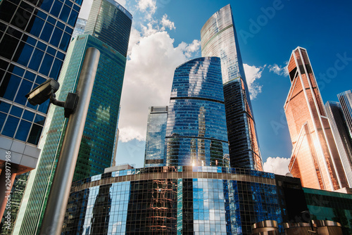 Photography Tall glass skyscrapers of business offices in city reflect blue sky, clouds, and other skyscrapers