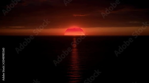 Serene ocean sunset with vibrant orange sun and gentle water reflection on horizon