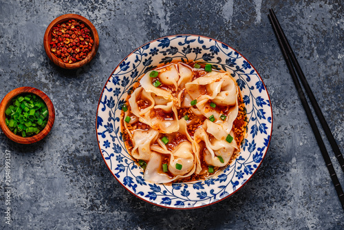 Wontons are placed in a bowl with spicy sauce.