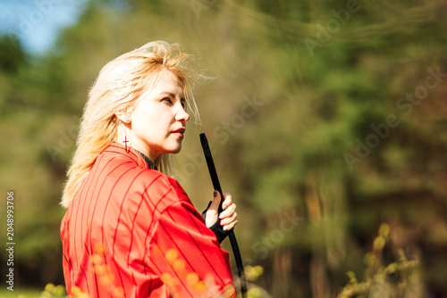 Slika na platnu young blonde woman in a red shirt stands in nature and holds a black mouthpiece