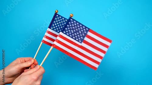 Hands holding two small American flags on blue background.