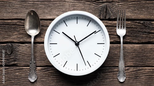 White clock face with spoon and fork on wooden background
