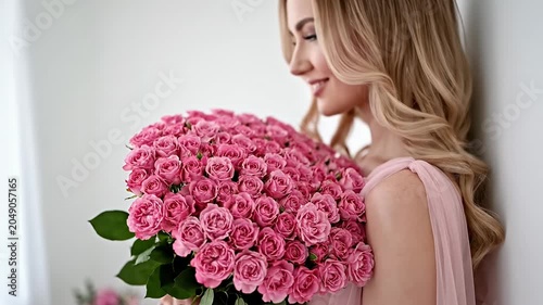 Blonde woman in pink dress holding a large rose bouquet.