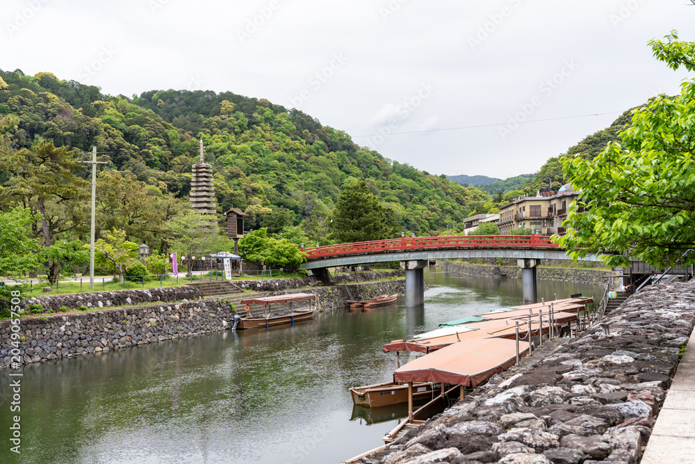Fototapeta premium Serene scene in Uji Japan, with red bridge, pagoda, boats and the river on a spring day