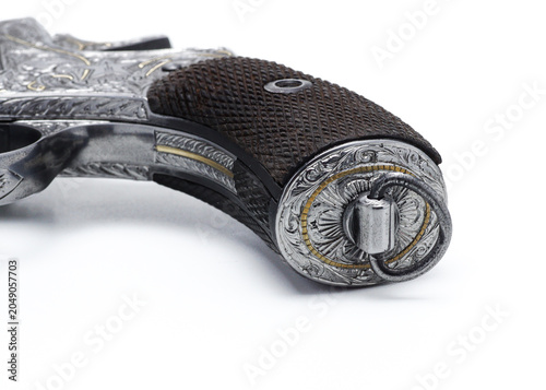 Fotografie Close-up product photograph of a vintage revolver handle featuring detailed hand engraving, textured grip panels, and fine metal craftsmanship, isolated on a white background
