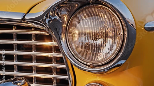 Chrome headlight and grill detail of yellow vintage car.