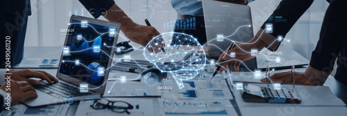 Fotografía This image captures a business meeting with professionals collaborating over laptops and data charts, featuring a digital brain graphic symbolizing innovative technology and analysis