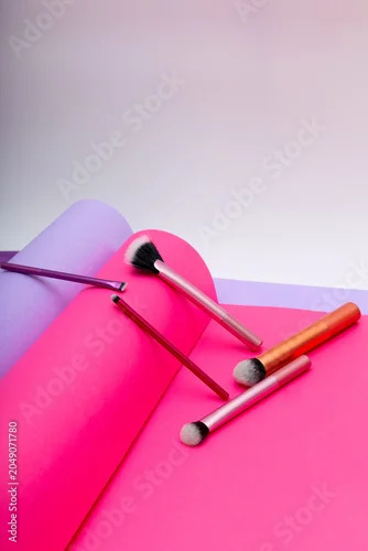 Fototapeta samoprzylepna Vibrant color papers and makeup brushes create an artful scene in a studio setting at daytime