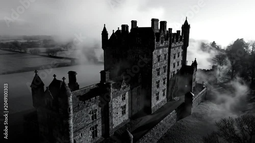 Epic aerial view of a majestic stone castle shrouded in dense fog in a spooky monochrome landscape.