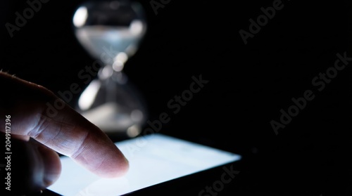 Wasting time scrolling on smartphone as sand flows through hourglass, digital distraction concept
