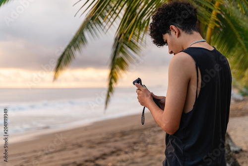Young man vlogging with camera on tropical beach at sunset