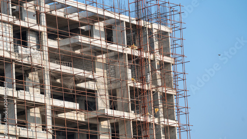 Fotografie Tall concrete building under construction covered in metal scaffolding against c
