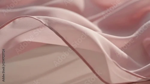 Soft pink fabric flows gently on a flat surface in sunlight in a calm indoor setting during the day