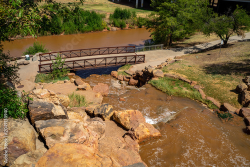 Waterfall On Red Brick and Red Rocks FLowing Under Bridge and Into River in Green Nature Park in Wichita Falls, Texas