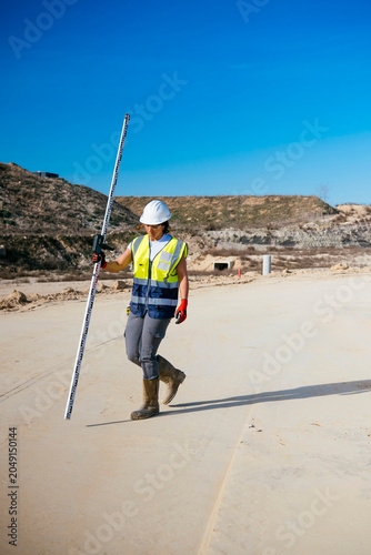 Woman construction worker surveying site with measuring rod