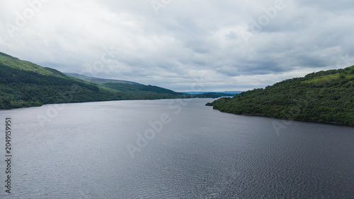 Obraz na płótnie Stunning panoramic view of Loch Lomond from Firkin Point, capturing the majestic scale of the lake flanked by lush green mountain slopes under a dramatic overcast sky