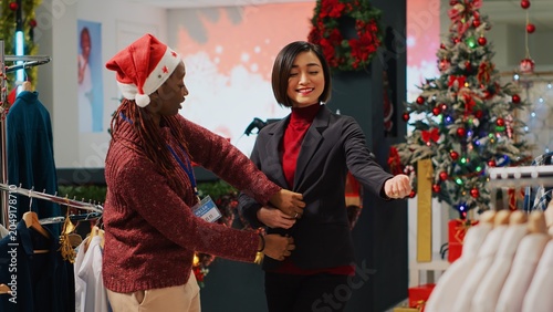 Canvastavla Customer happy with perfectly fitting elegant blazer after trying it on, asking worker for opinion in Christmas decorated fashion store