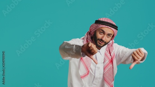 Tableau sur toile Arabic person in historic dress and kufiyah gives thumbs down and indicates discontent with what he sees