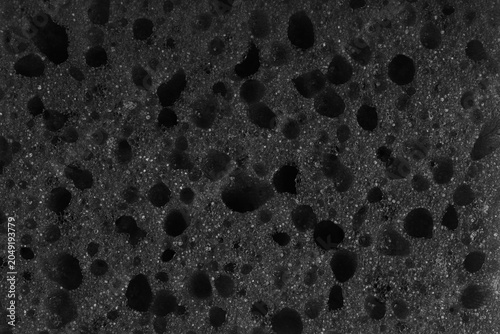 Macro, closeup of black foam sponge texture with porous, spongy and bubbly surface pattern suitable for abstract background design. Foamed polyurethane material surface