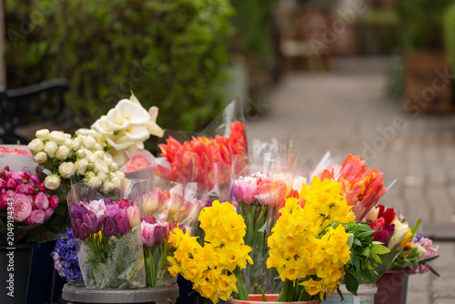 Small flower bouquets displayed for sale on a busy street, colorful fresh blossoms arranged by vendor, urban marketplace atmosphere, seasonal floral trade, and outdoor commerce concept.