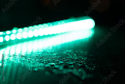 Raindrops on a dark surface reflecting blurred linear bokeh lights