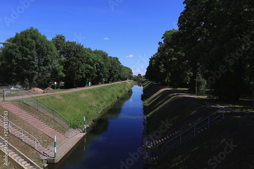 Blick entlang des baumbestandenen Kanals zur Schleuse mit Radweg und Spiegelung im Wasser, Merseburg, Saalekreis, Sachsen-Anhalt, Deutschland