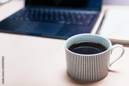 A close-up of a cup of coffee in front of a workspace.