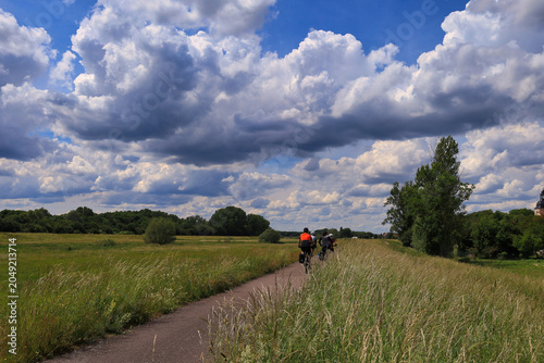 Radfahrer auf dem Elster-Radweg durch eine idyllische Wiesenlandschaft unter einem spektakulären Wolkenhimmel, Ermlitz, Schkopau, Saalekreis, Sachsen-Anhalt, Deutschland