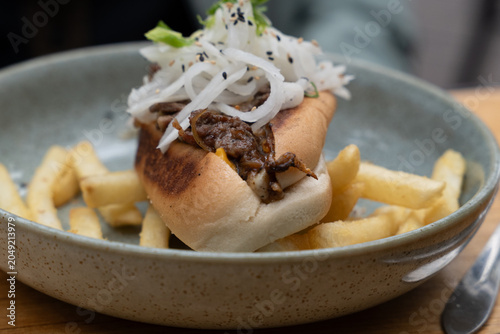 Gourmet beef sandwich topped with pickled radish onions beside french fries