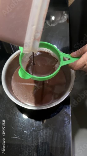 Hand Straining Ground Chocolate Into Boiling Pot on Kitchen Stove