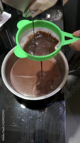 Hand Straining Ground Chocolate Into Boiling Pot on Kitchen Stove