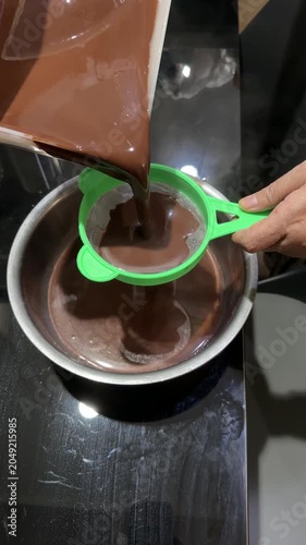 Hand Straining Ground Chocolate Into Boiling Pot on Kitchen Stove