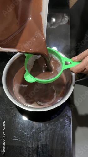 Hand Straining Ground Chocolate Into Boiling Pot on Kitchen Stove