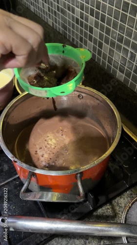Hand Straining Ground Chocolate Into Boiling Pot on Kitchen Stove