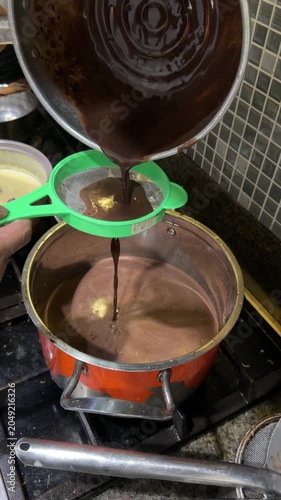 Hand Straining Ground Chocolate Into Boiling Pot on Kitchen Stove