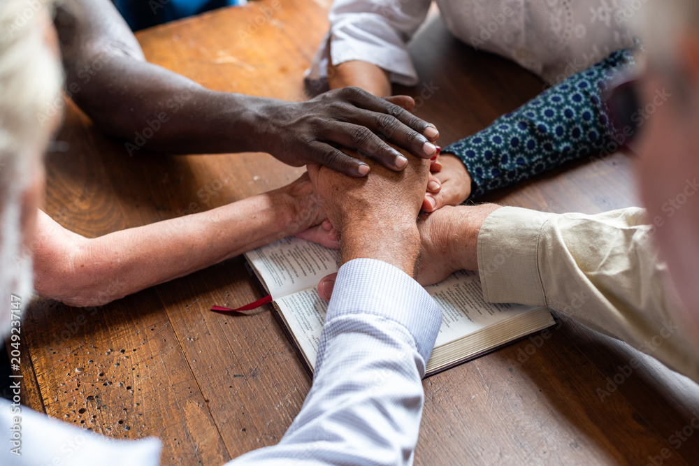 Naklejka premium Diverse group holding hands over a book on a wooden table.