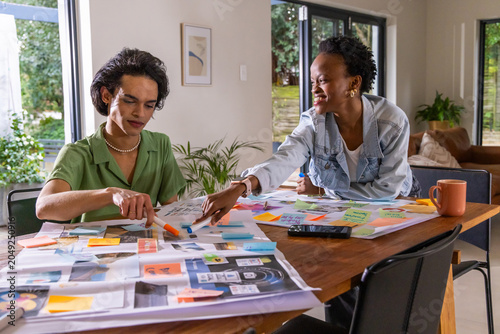 Diverse coworkers collaborating at dining table, arranging layouts with markers, smartphone, mug