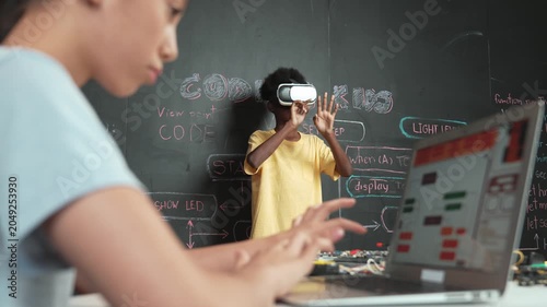 Closeup of school girl hand coding program while african student using VR interact with metaworld. Smart boy wearing virtual reality glasses and playing video games at innovative class. Edification