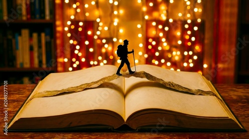 A miniature hiker figurine walking across an open antique book with magical fairy light bokeh background.