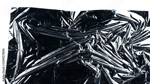 Macro eye level shot of a heavily wrinkled and creased black plastic foil texture reflecting light.