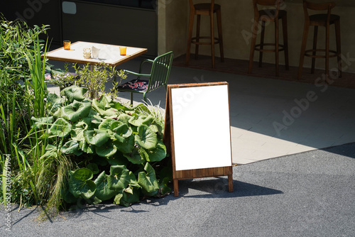 Blank white outdoor advertising stand sandwich board mock up template. Clear street signage board placed by an outdoor dinning area of a restaurant.
