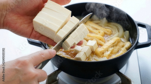 湯気の立つ味噌汁に豆腐を加える手元、温かい和食の準備風景