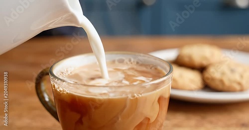 Pouring milk into a cup of coffee with cookies on the side, a perfect morning beverage.