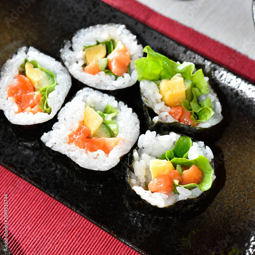 Homemade roll sushi on black plate on table.