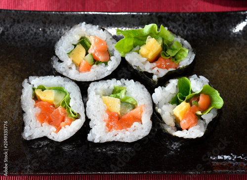 Homemade roll sushi on black plate on table.