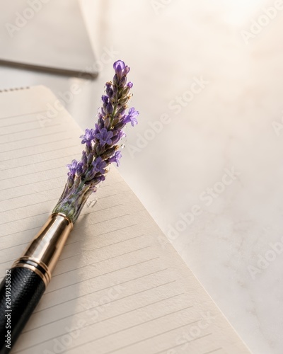 Conceptual Close-up of a Professional Fountain Pen with Blooming Lavender Flower Nib on a Notebook with Soft Morning Light and Negative Space